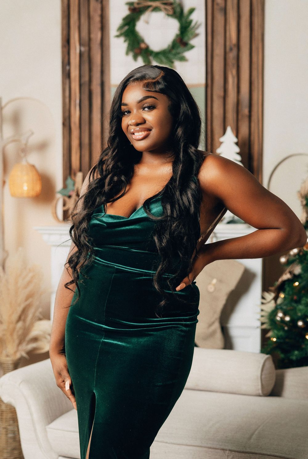 Smiling woman in green velvet dress poses confidently in beautifully decorated Christmas setting.