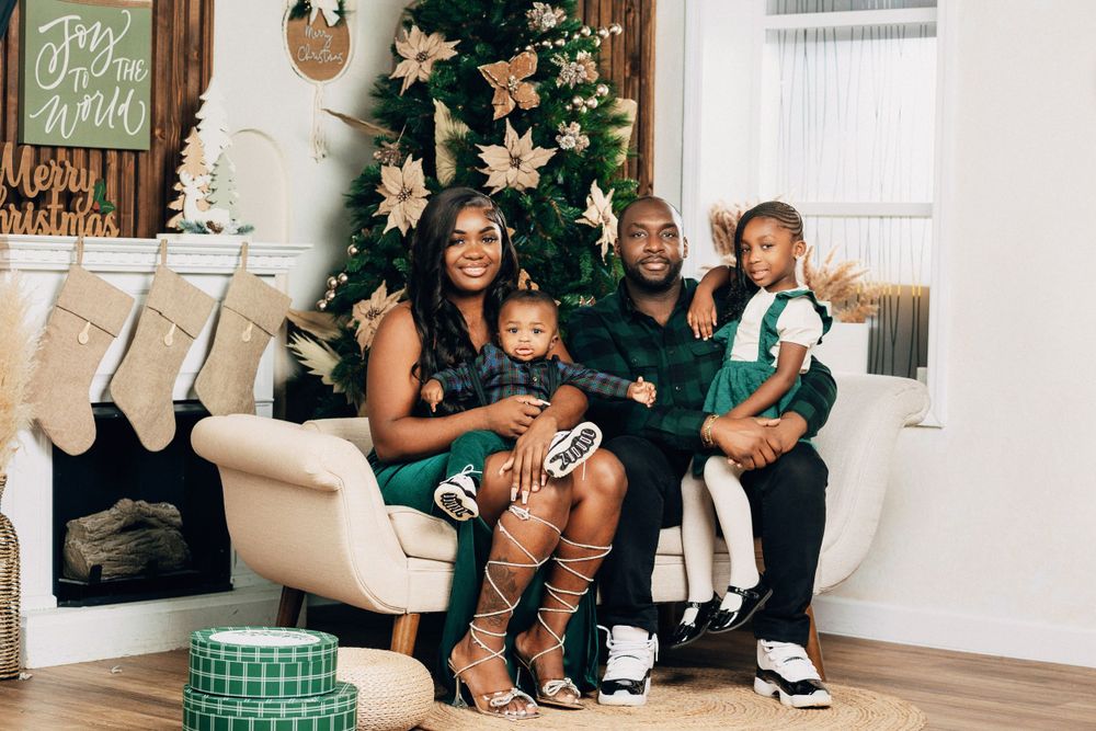 Happy family of four smiling together in front of decorated Christmas tree with gifts.