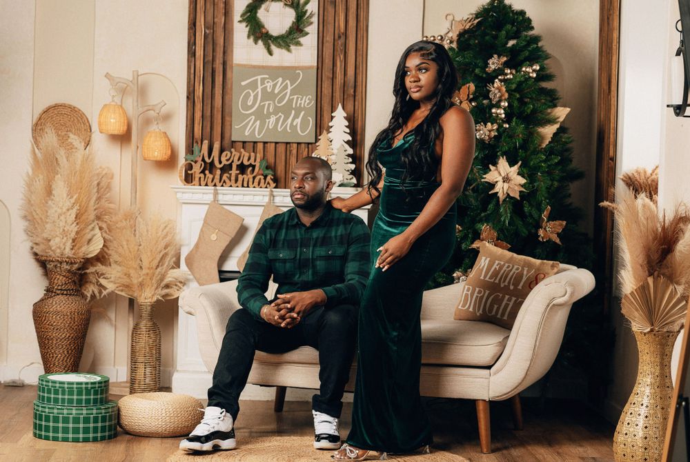 Couple posing together near Christmas tree with festive holiday decorations and warm lighting.