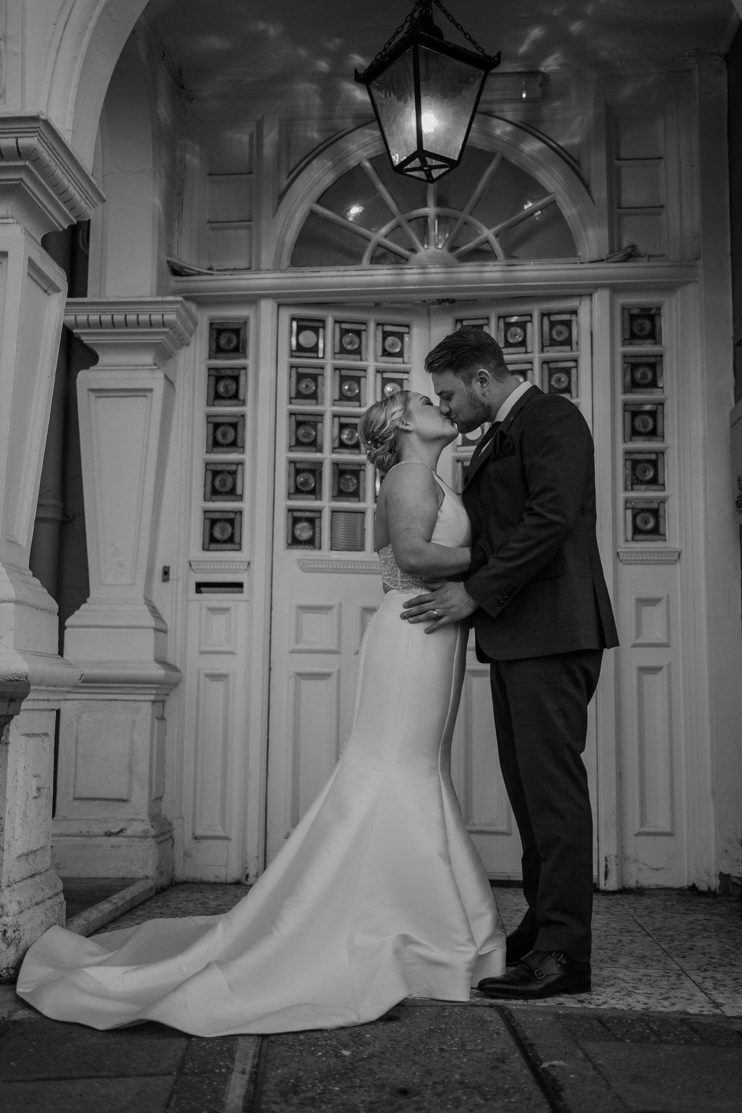 Bride and groom in a black and white photo kissing outside their wedding venue.
