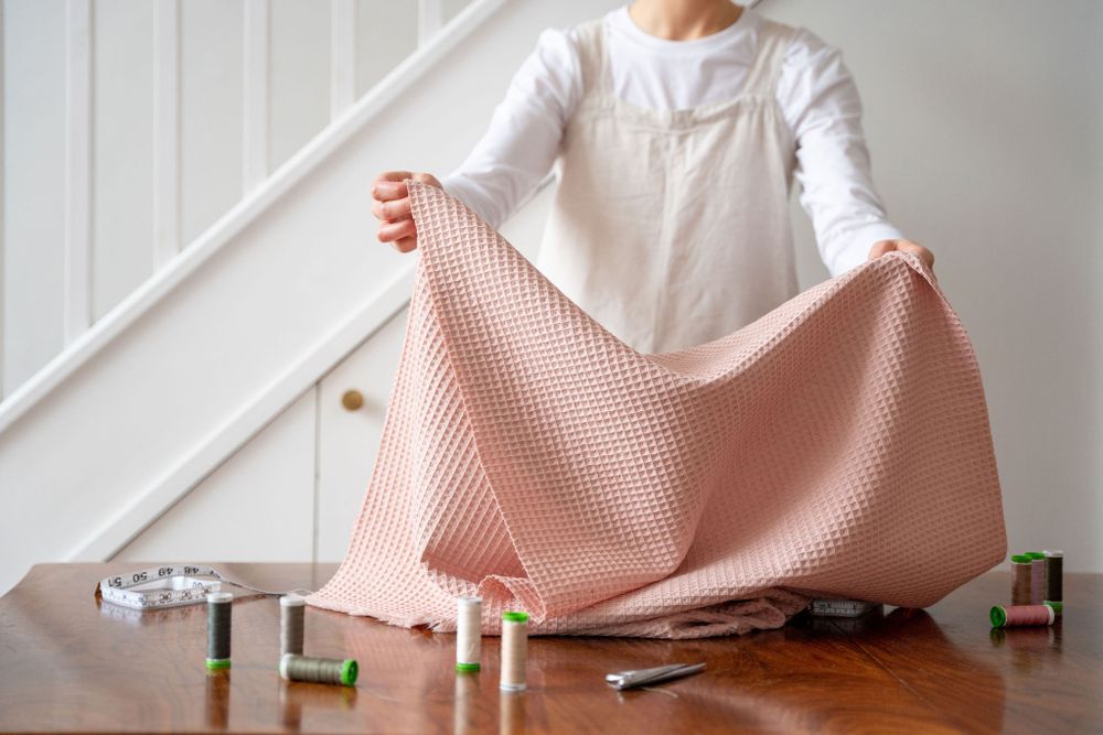 Person holding pink knitted textile on wooden table with sewing supplies.