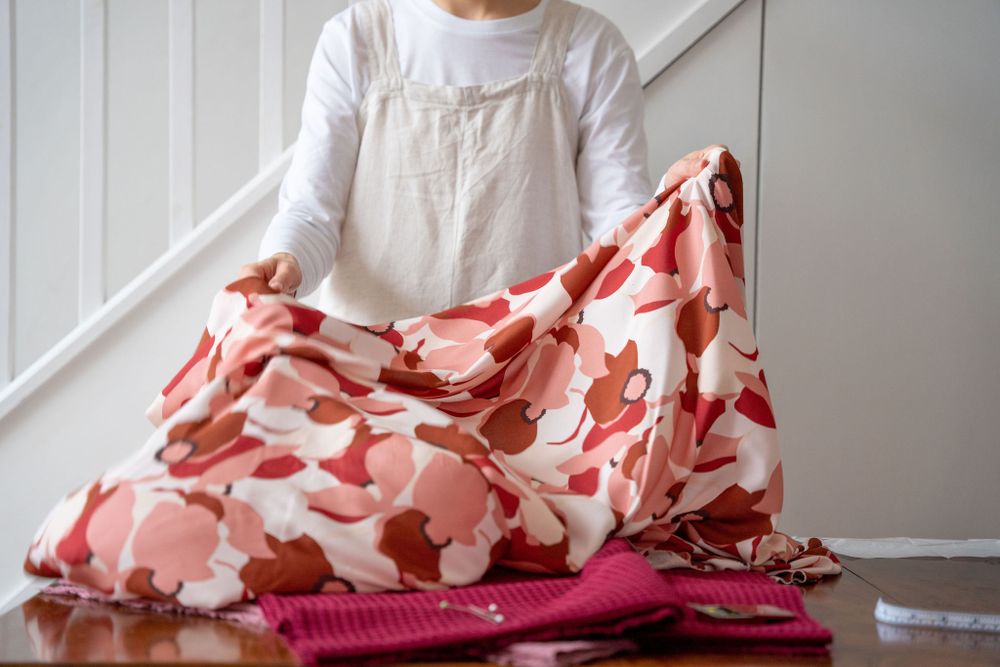 Hands displaying floral patterned fabric on wooden surface with sewing materials.