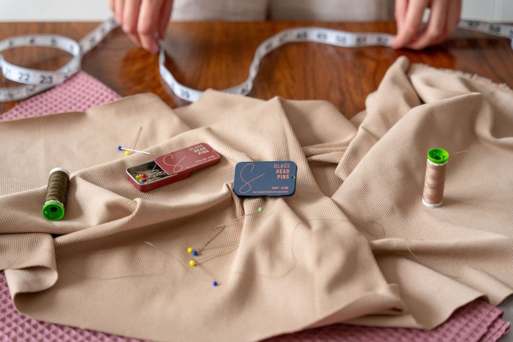 Sewing supplies and measuring tape arranged on beige fabric workspace.