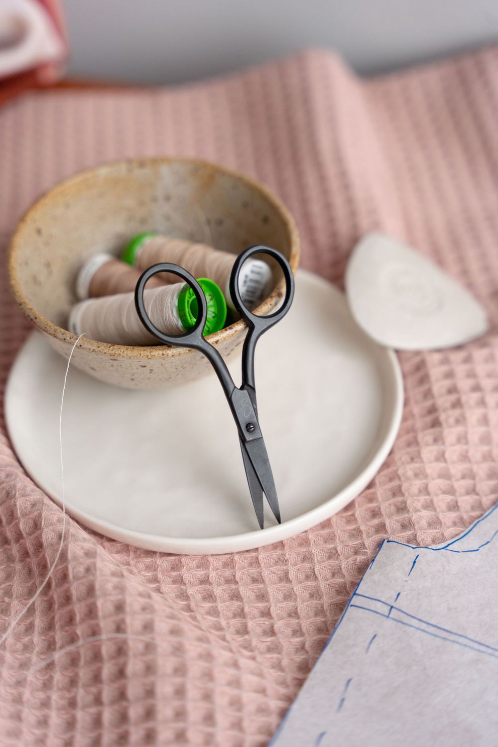 Scissors and sewing tools placed on pink textured fabric with pattern paper visible.