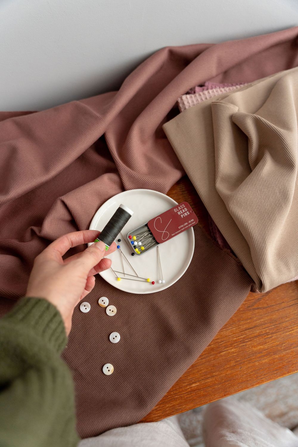 Hands placing buttons on brown fabric laid out on wooden surface.