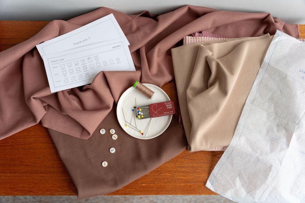 Brown fabric with buttons arranged on wooden surface next to sewing supplies.