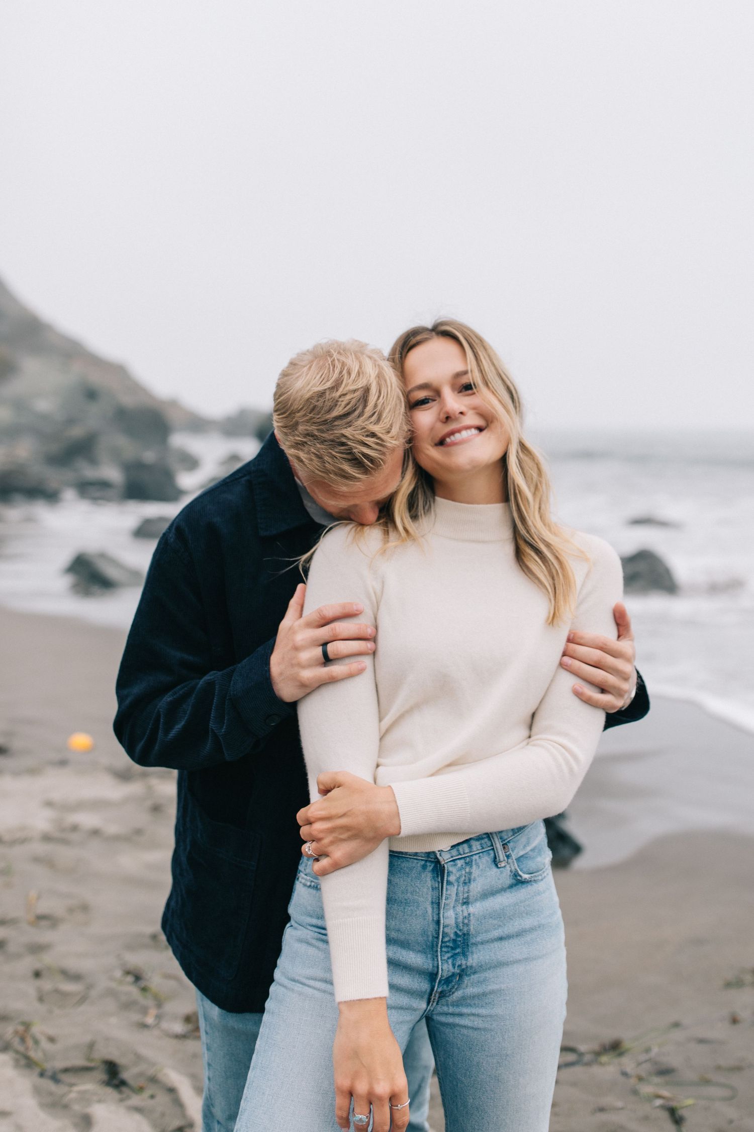 Candid romantic moment between couple on misty coastal beach.