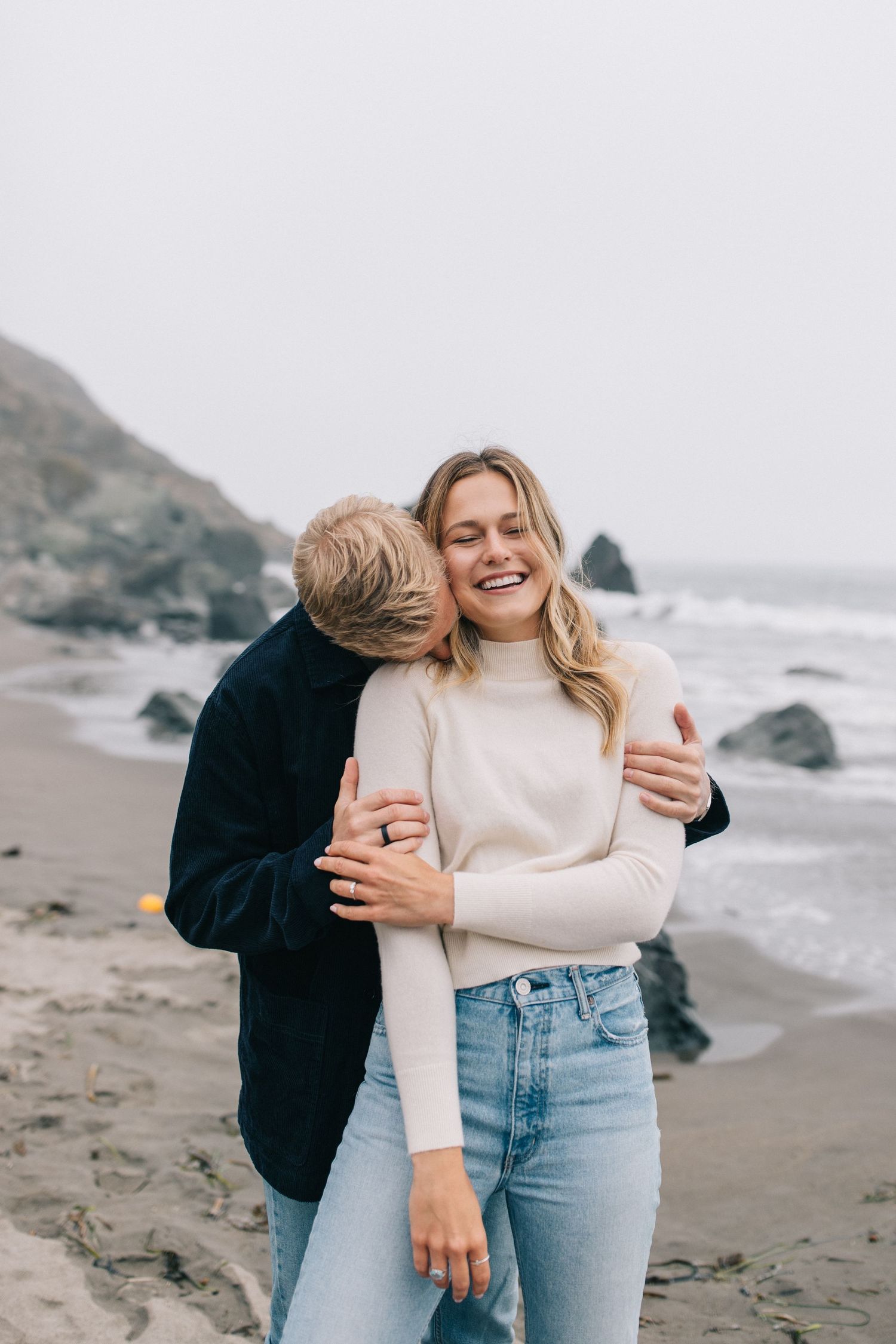 Romantic moment between couple in casual attire on foggy beach.