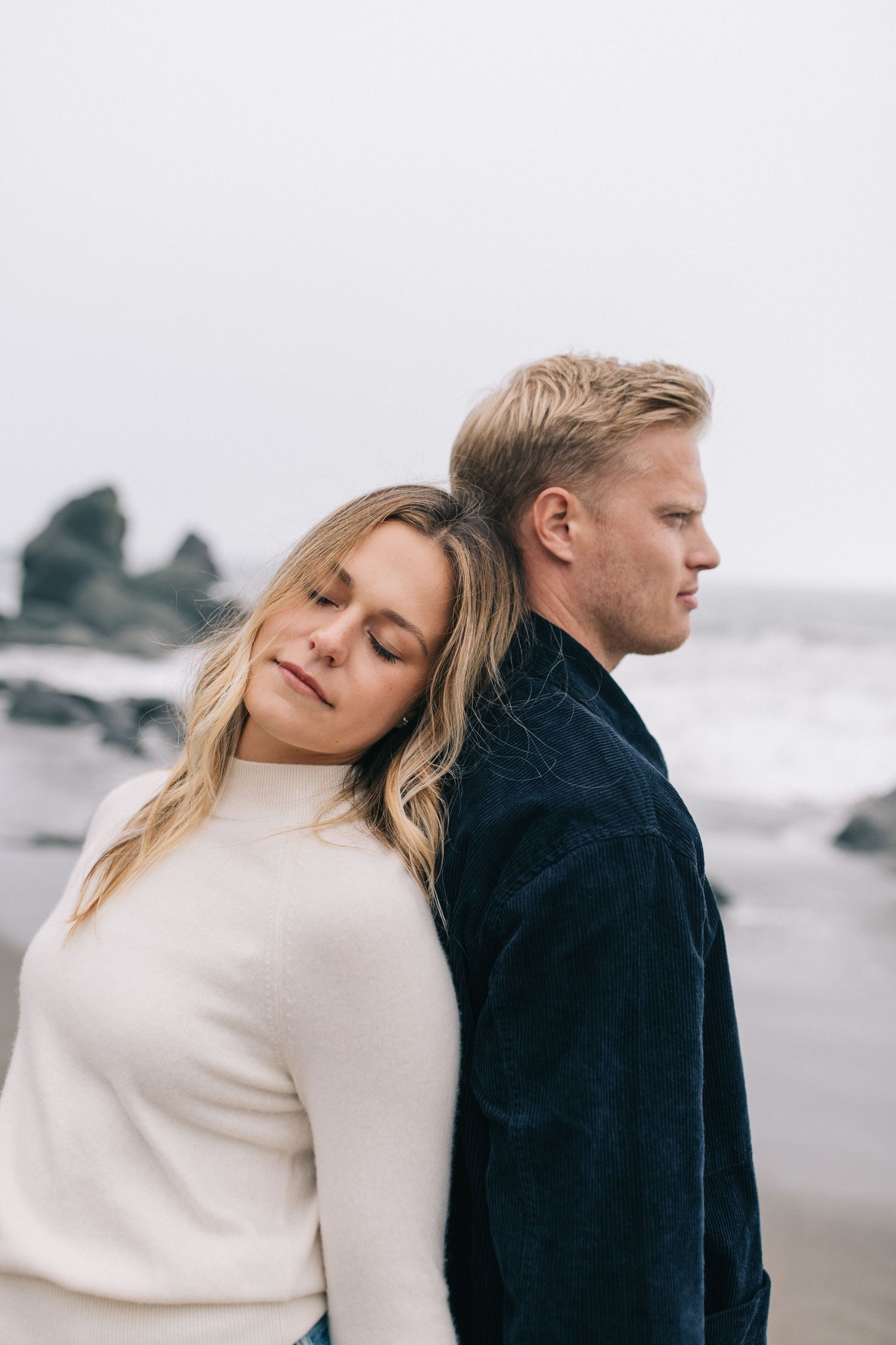 Intimate portrait of couple in cozy sweaters standing close on foggy beach.