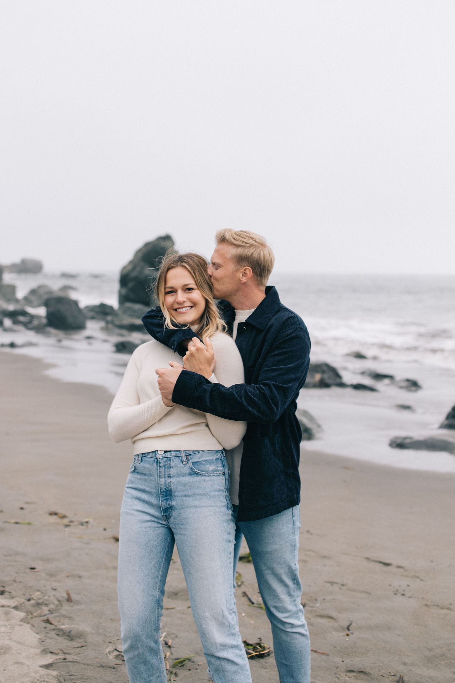 Candid moment of laughter and joy during coastal photoshoot on overcast day.