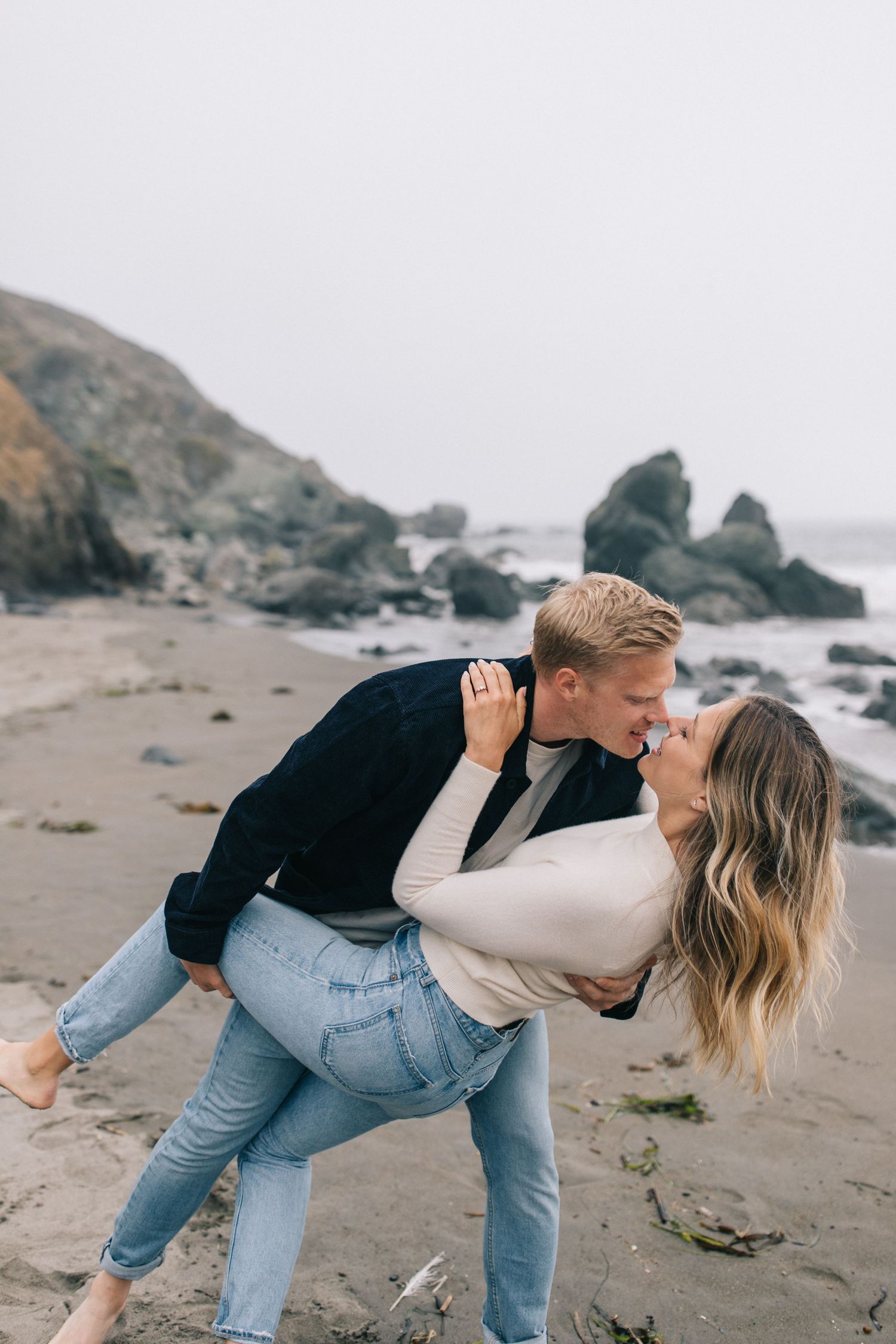 Playful beach photoshoot moment with couple dancing by the ocean.