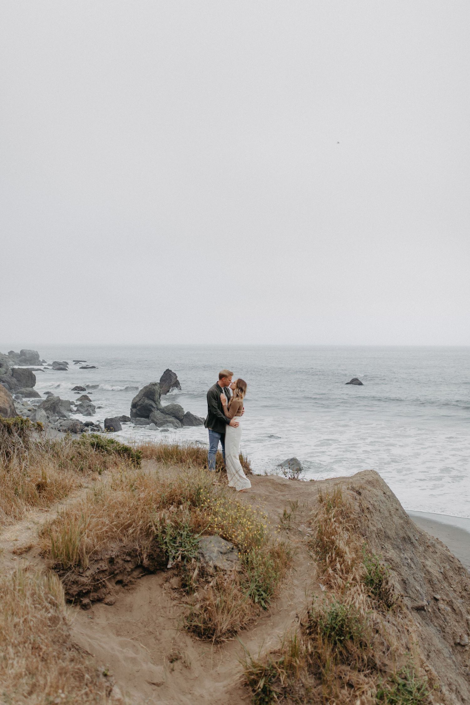 Intimate moment captured of couple standing on California coastal cliffs with dramatic ocean views.