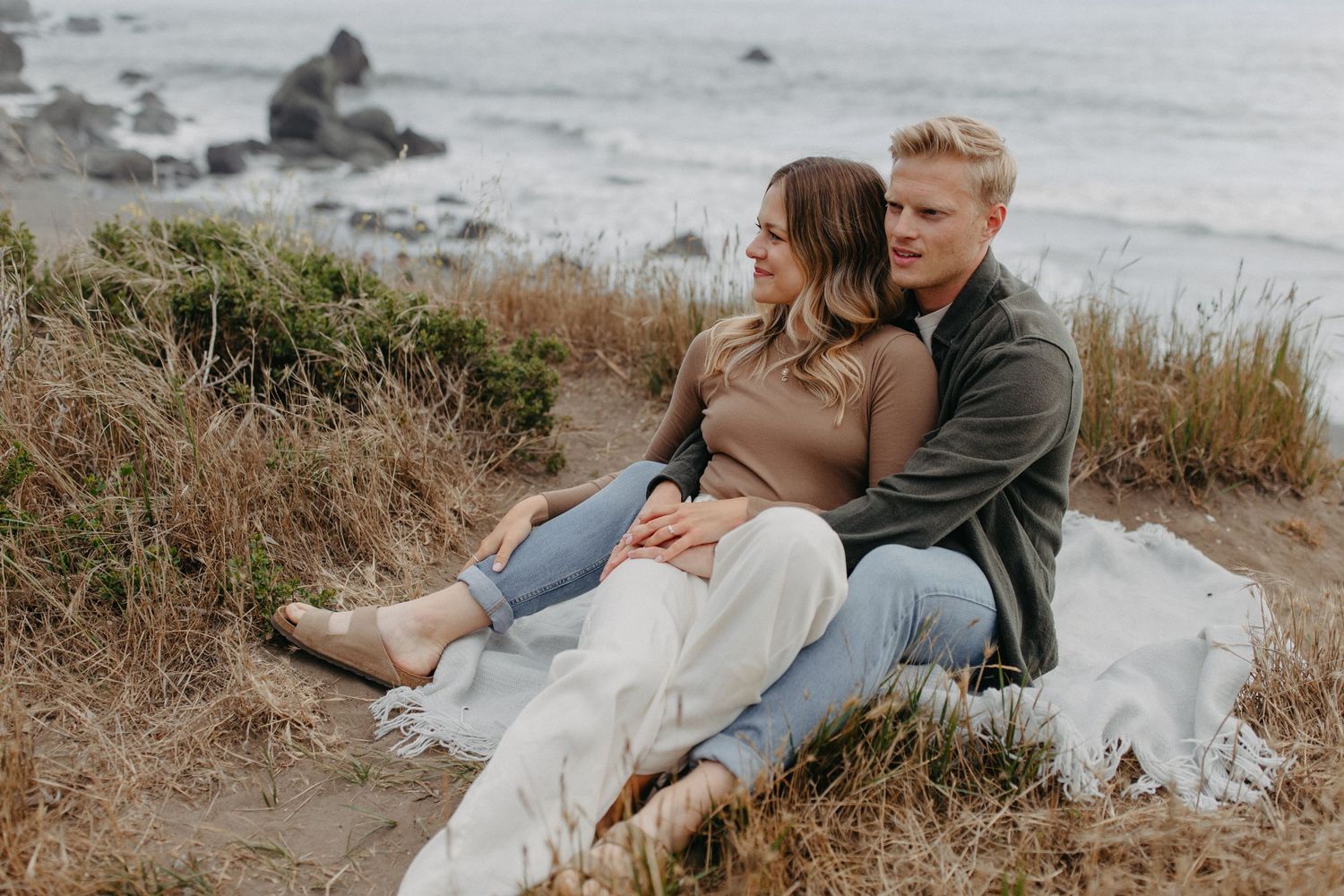 Couple relaxing together on blanket overlooking rocky coastline during sunset.