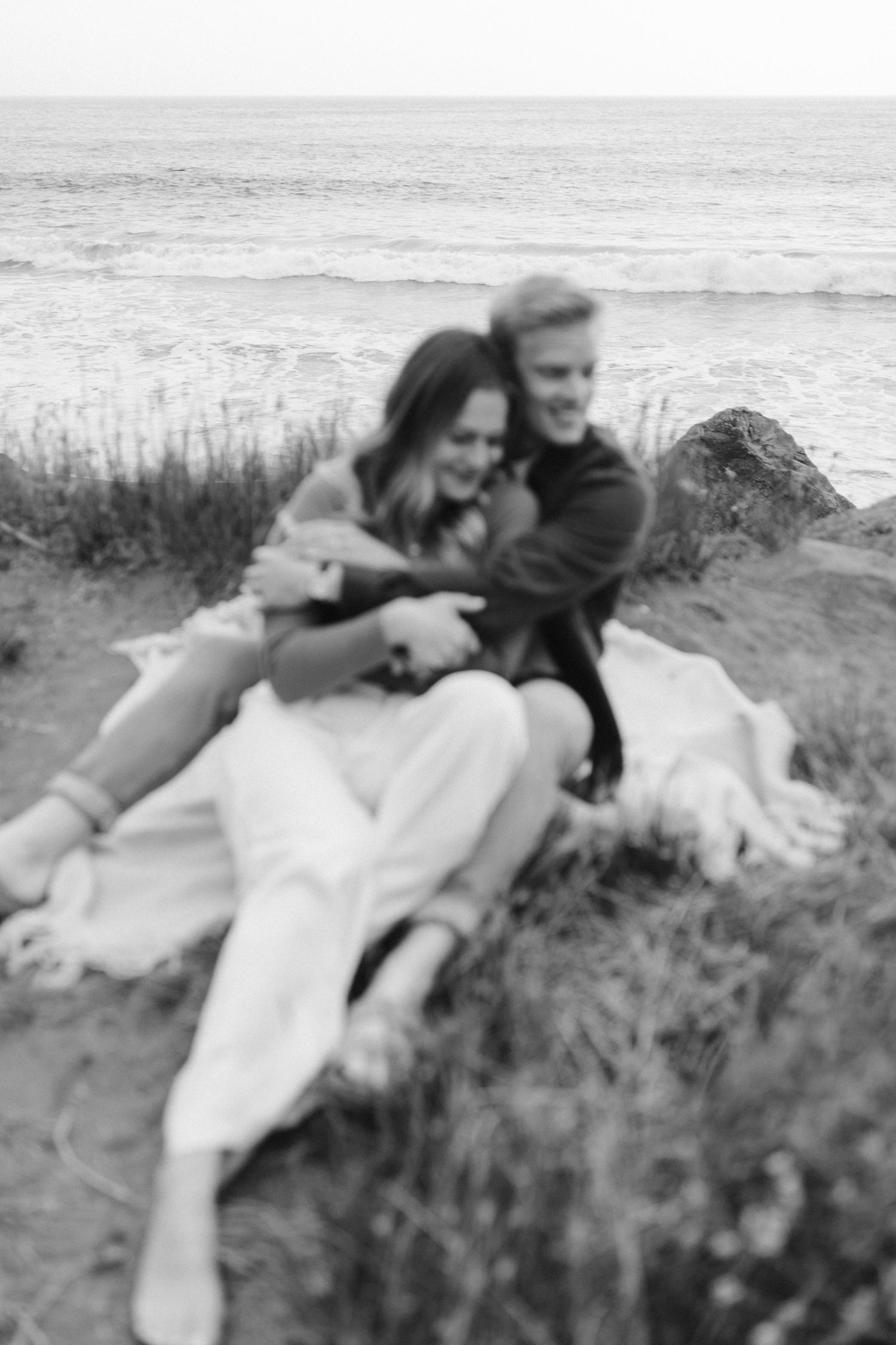 Black and white portrait of couple embracing on seaside cliff.
