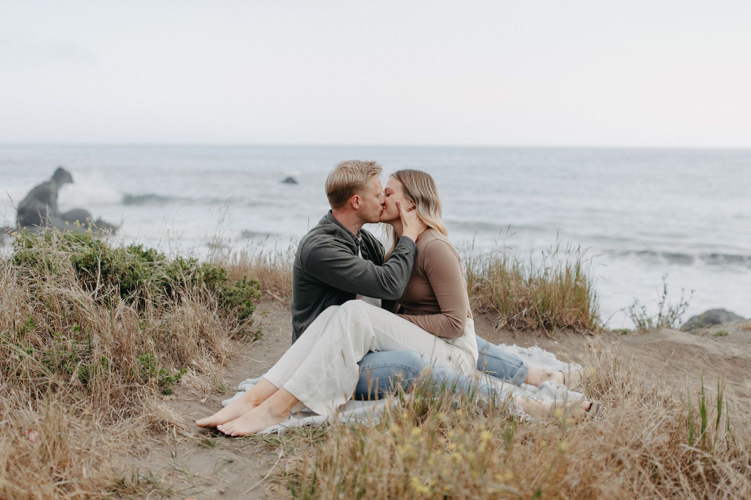 Couple sharing romantic moment on coastal bluff with rocks and ocean in distance.