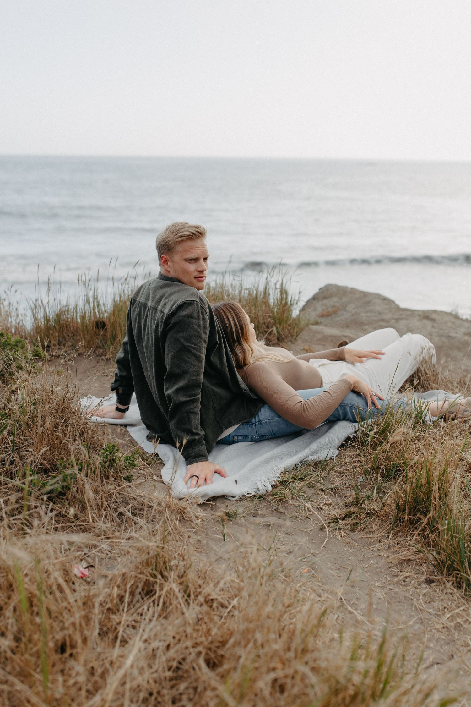 A couple relaxing together on a blanket near the ocean coast during sunset.