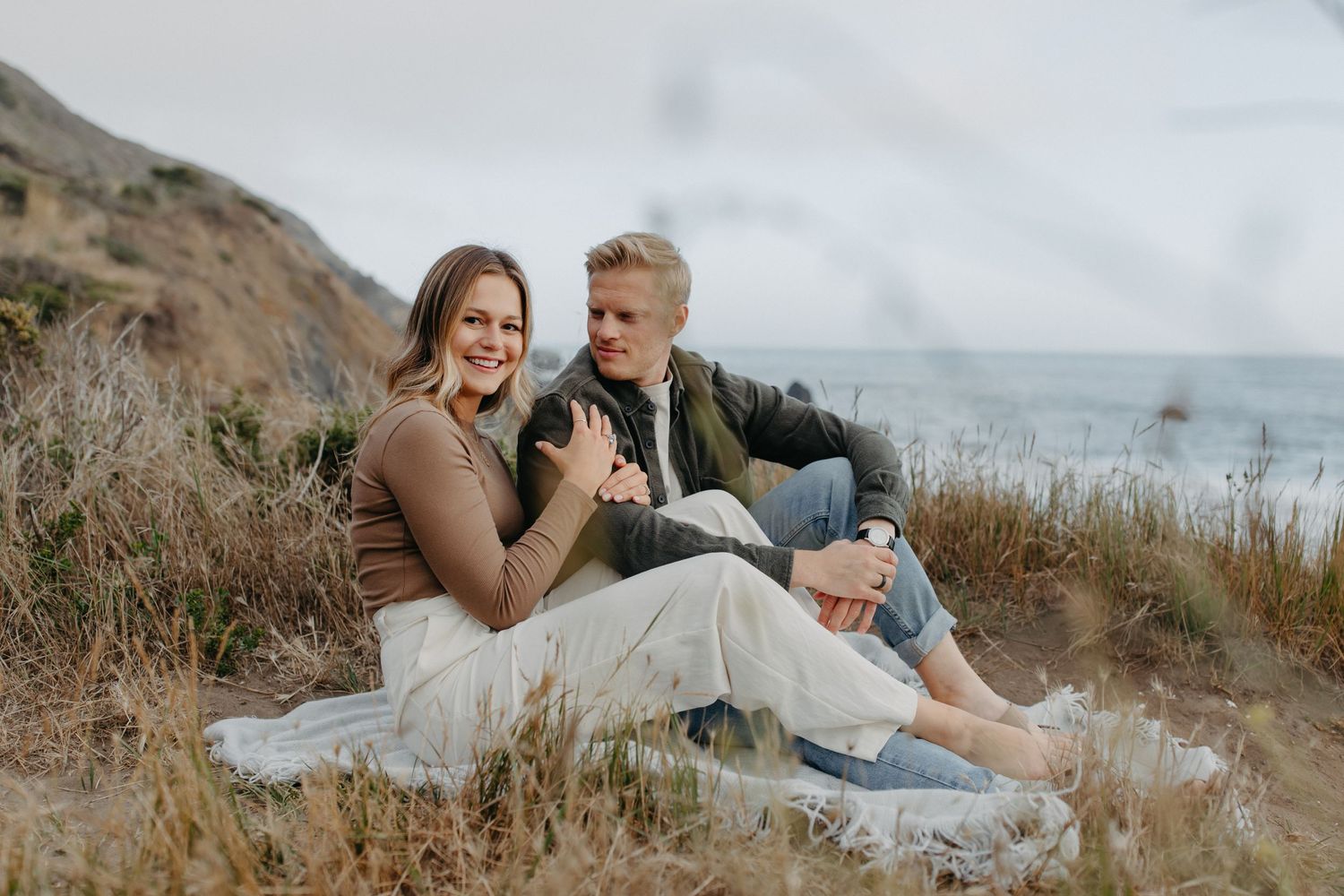 A romantic moment shared between two people on a coastal hillside.