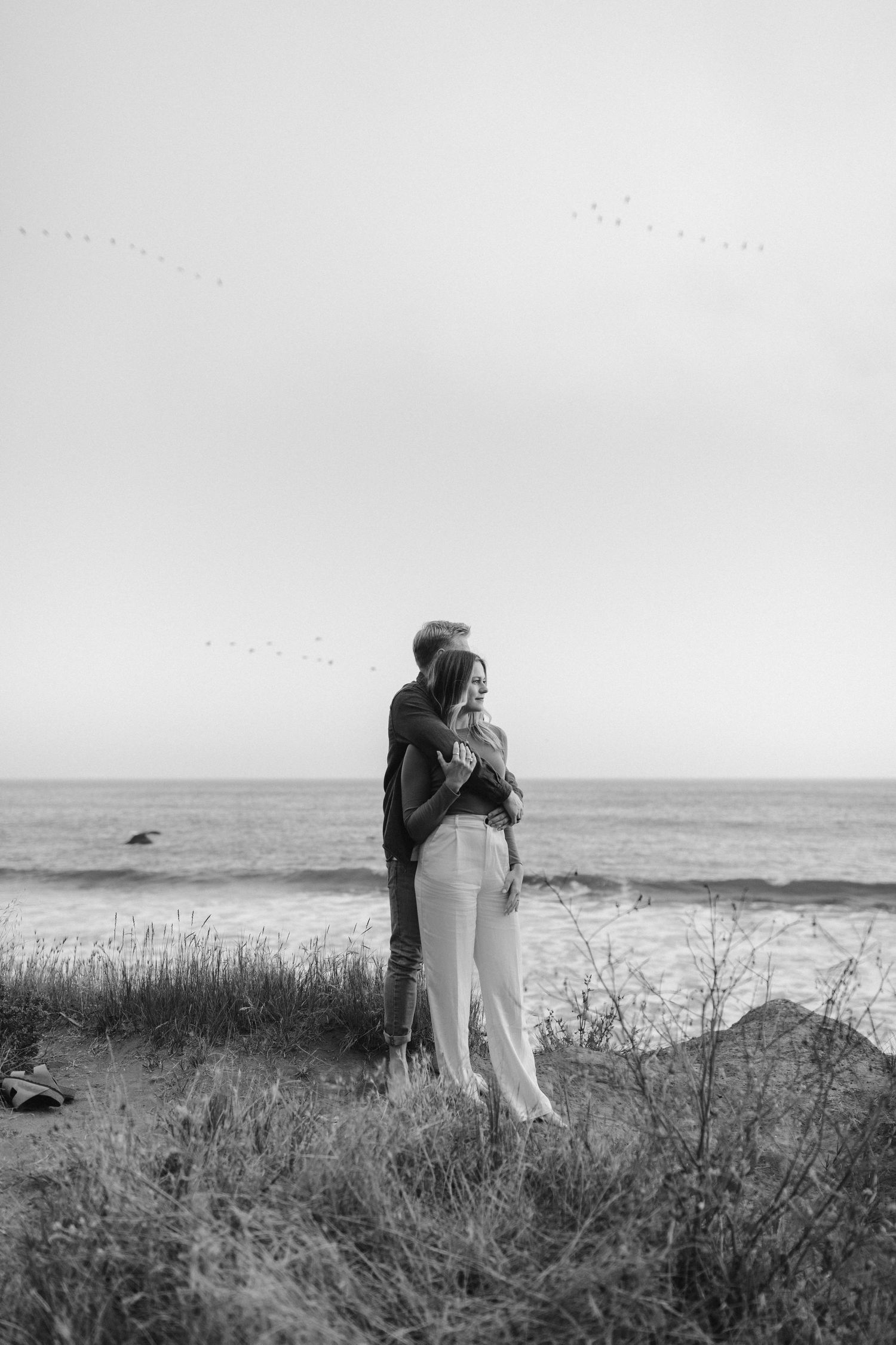 A black and white photograph of a couple embracing on a coastal cliff.