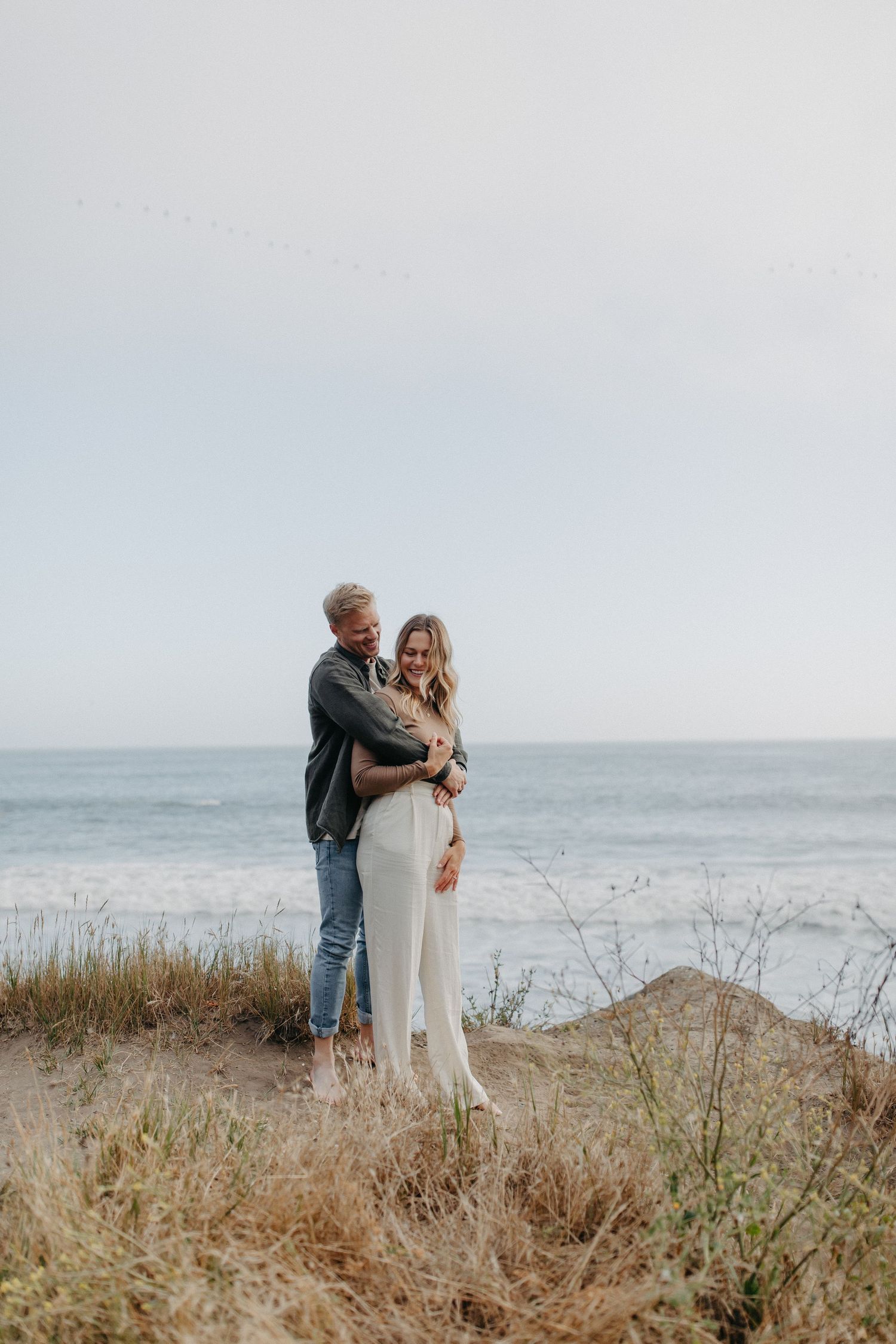 A couple sharing a tender moment on a coastal cliff during golden hour.