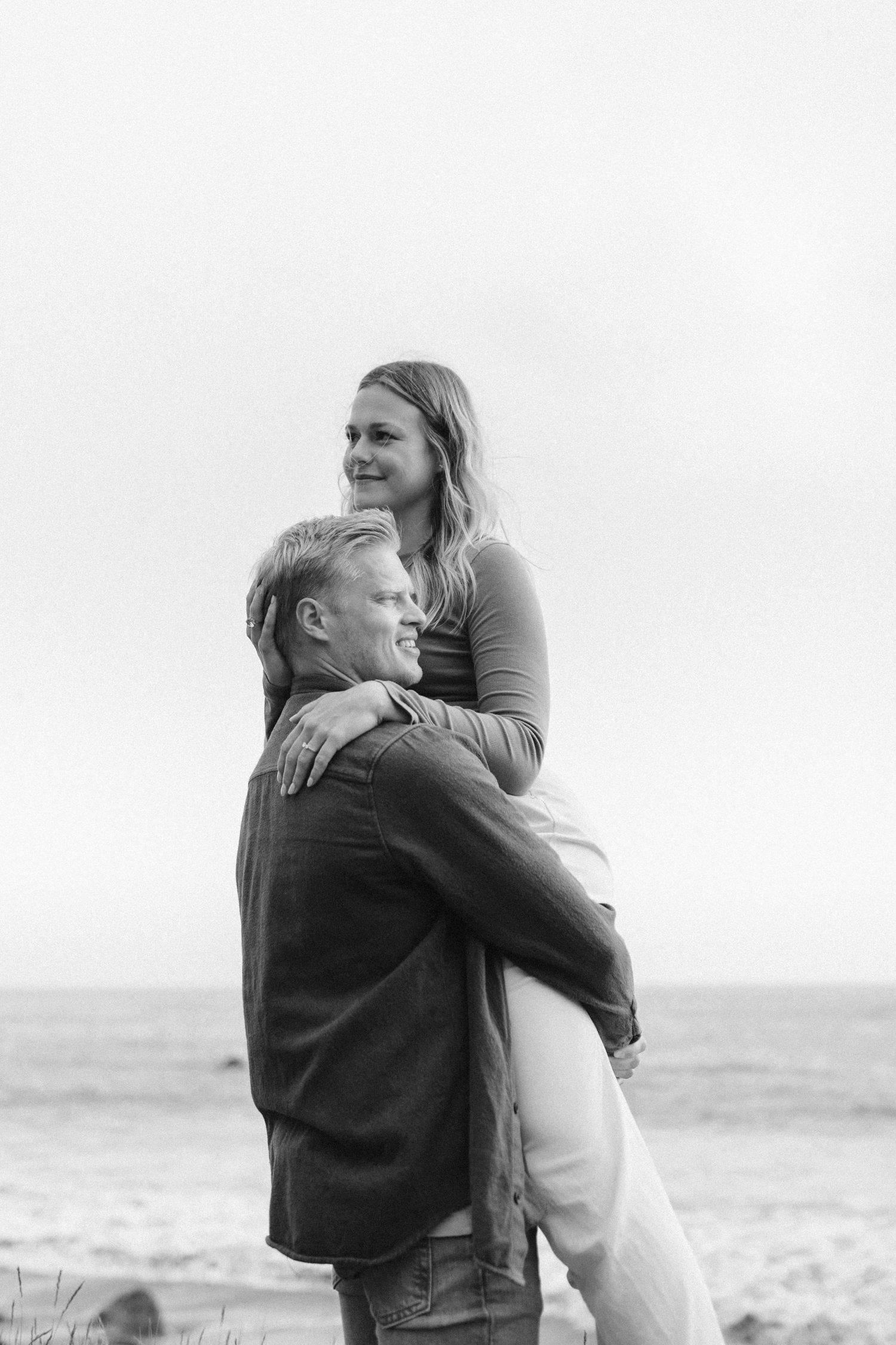 A black and white portrait of two people sharing an intimate moment by the sea.