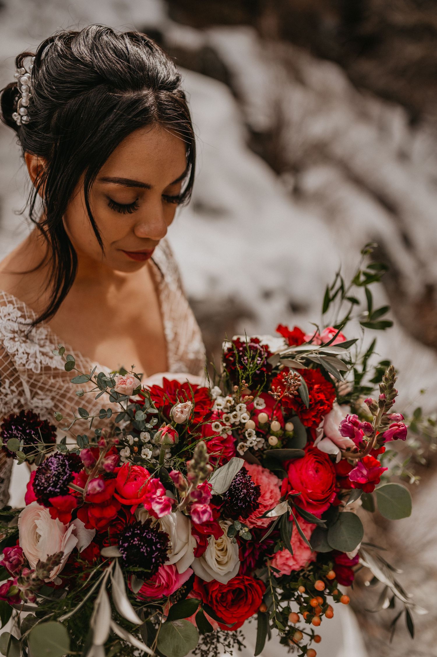 A stunning bridal bouquet features deep red roses and burgundy flowers with lush greenery.