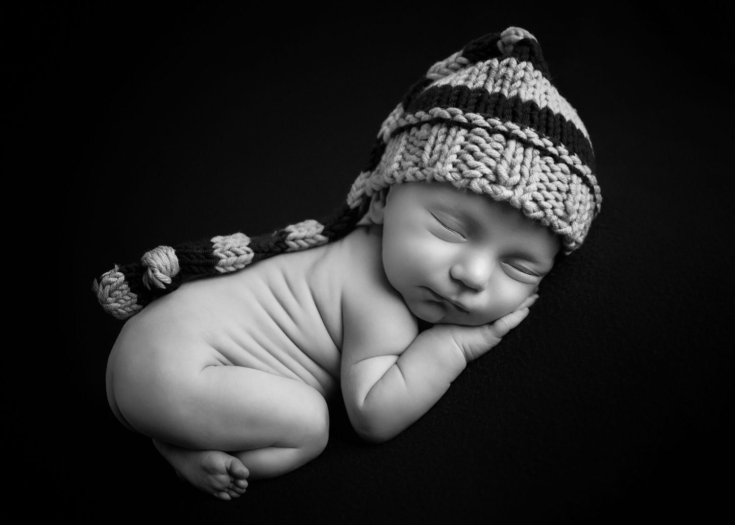 Black and white image of naked baby in bum up pose with woolly hat for newborn photoshoot