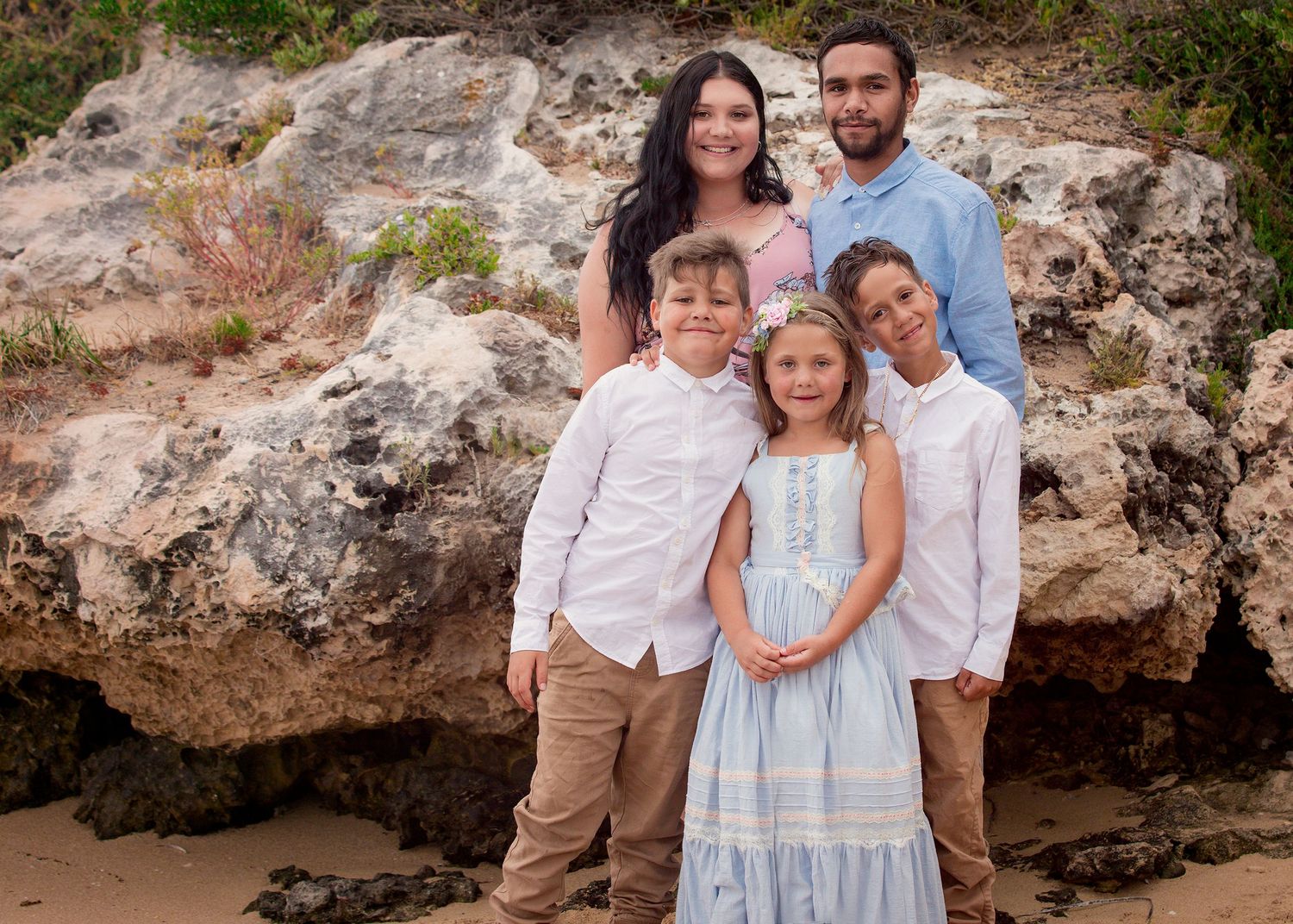 Family of 2 boys, a girl and their parents at the beach in front of sandstone boulders at Point Peron Rockingham