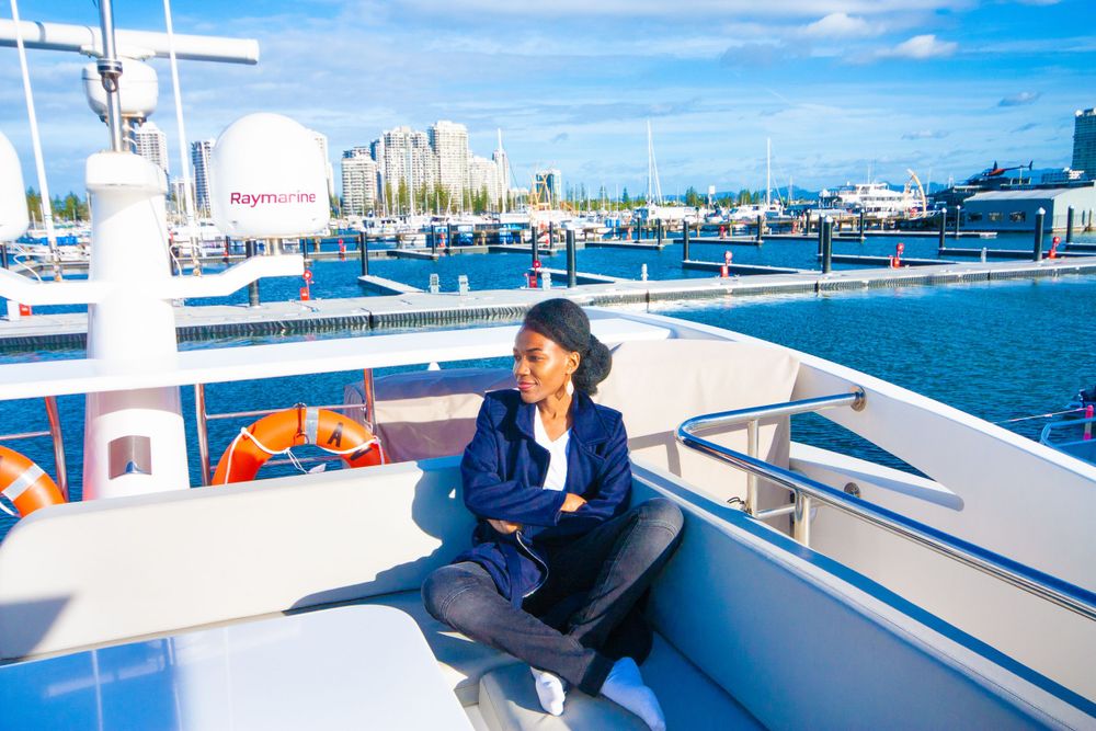 Person relaxing on a yacht deck with blue ocean and city skyline in the background on a sunny day.