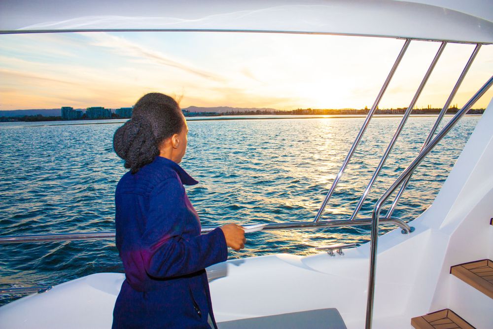 A person watches the sunset from a yacht with golden light reflecting on the water.