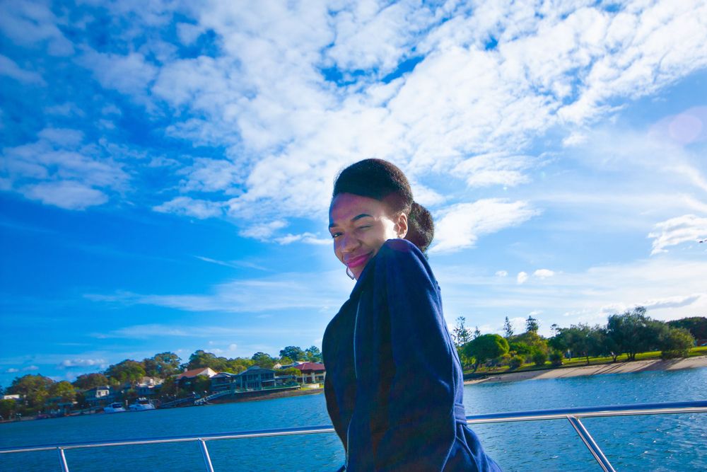Person enjoying the ocean breeze on a boat deck against blue sky and waterfront scenery.
