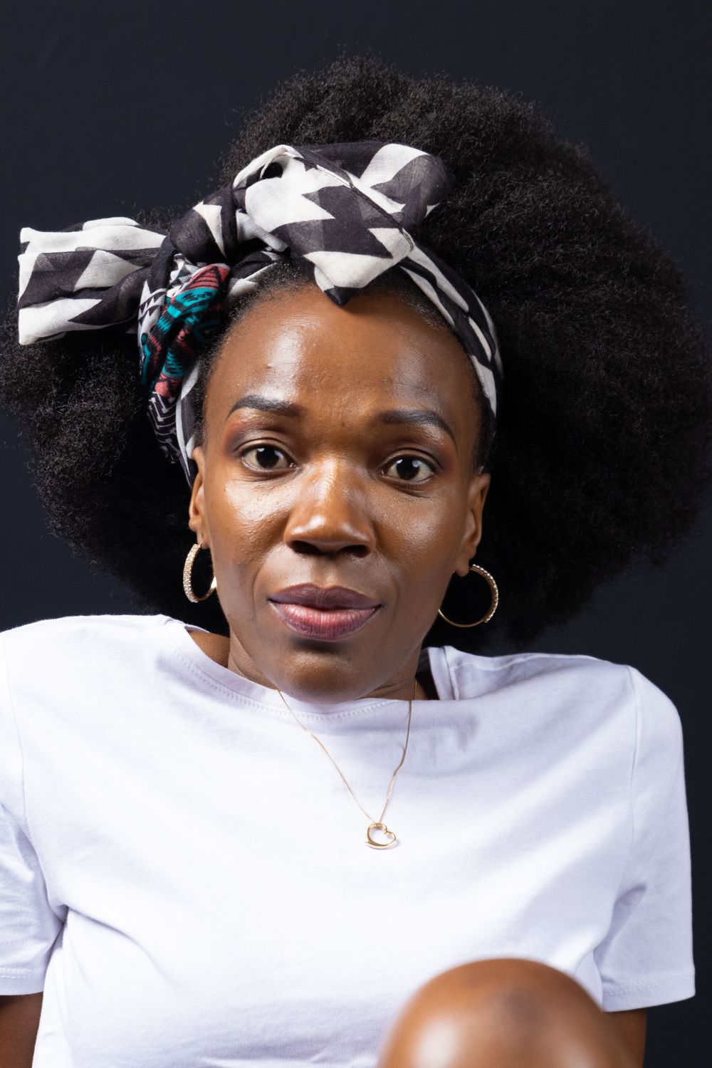 Portrait wearing white t-shirt and geometric black and white headwrap with natural hair.