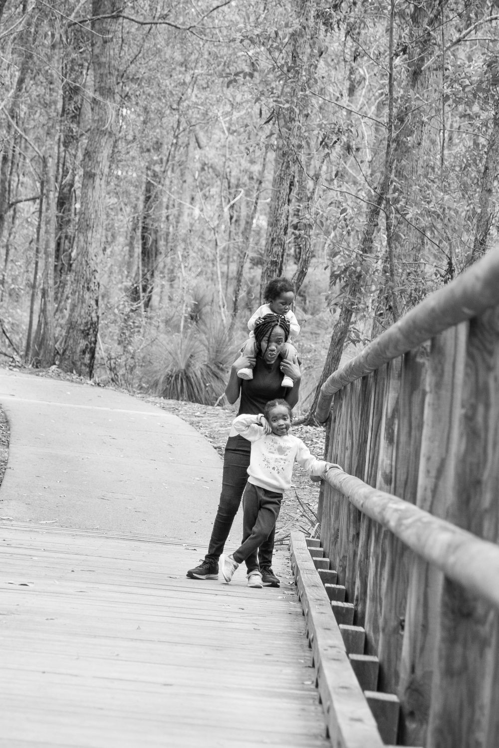 Black and white photo of people walking on a wooden boardwalk through a forest.