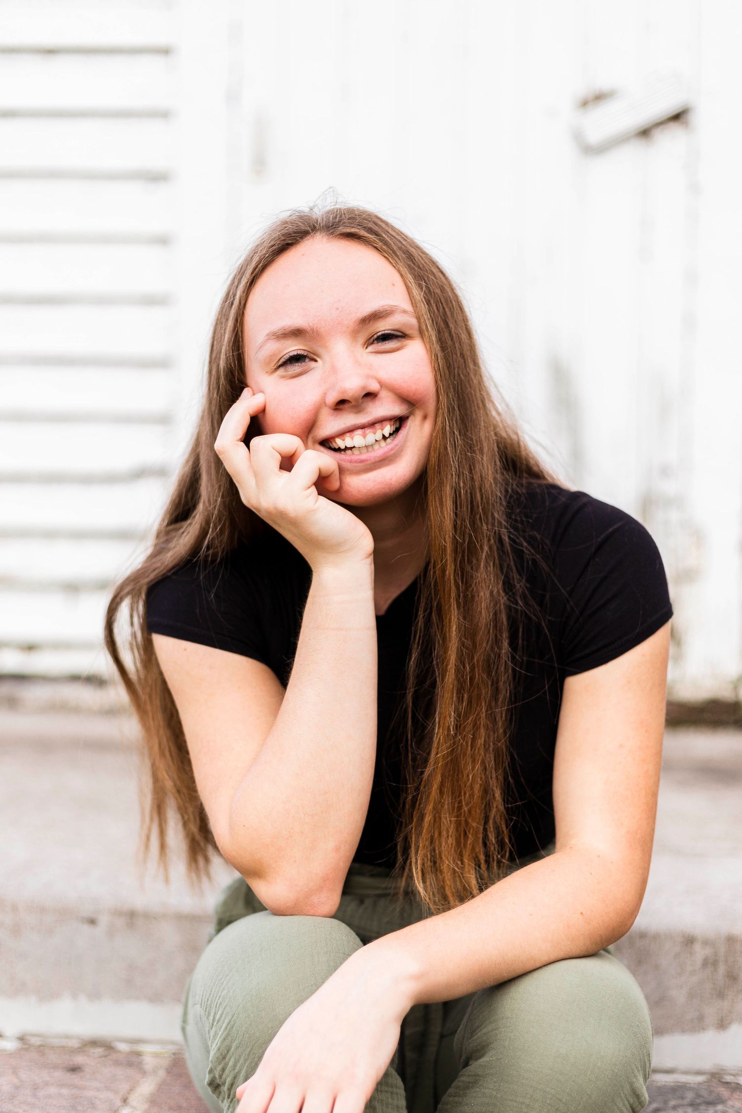 Smiling girl with long brown hair. holding her cheek and laughing at the camera