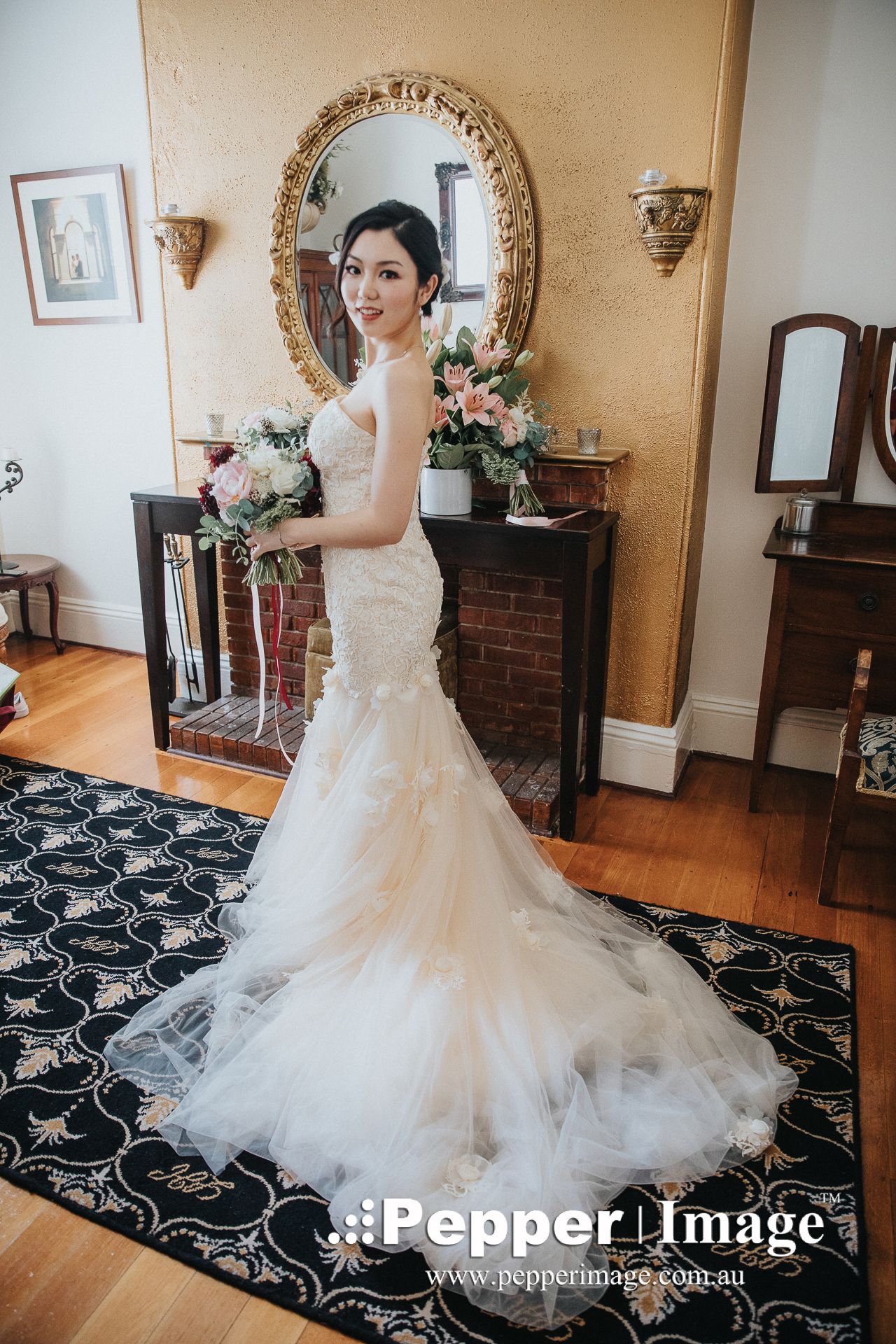 Bride in a fitted mermaid lace wedding gown holding a bouquet in a classic ornate interior.