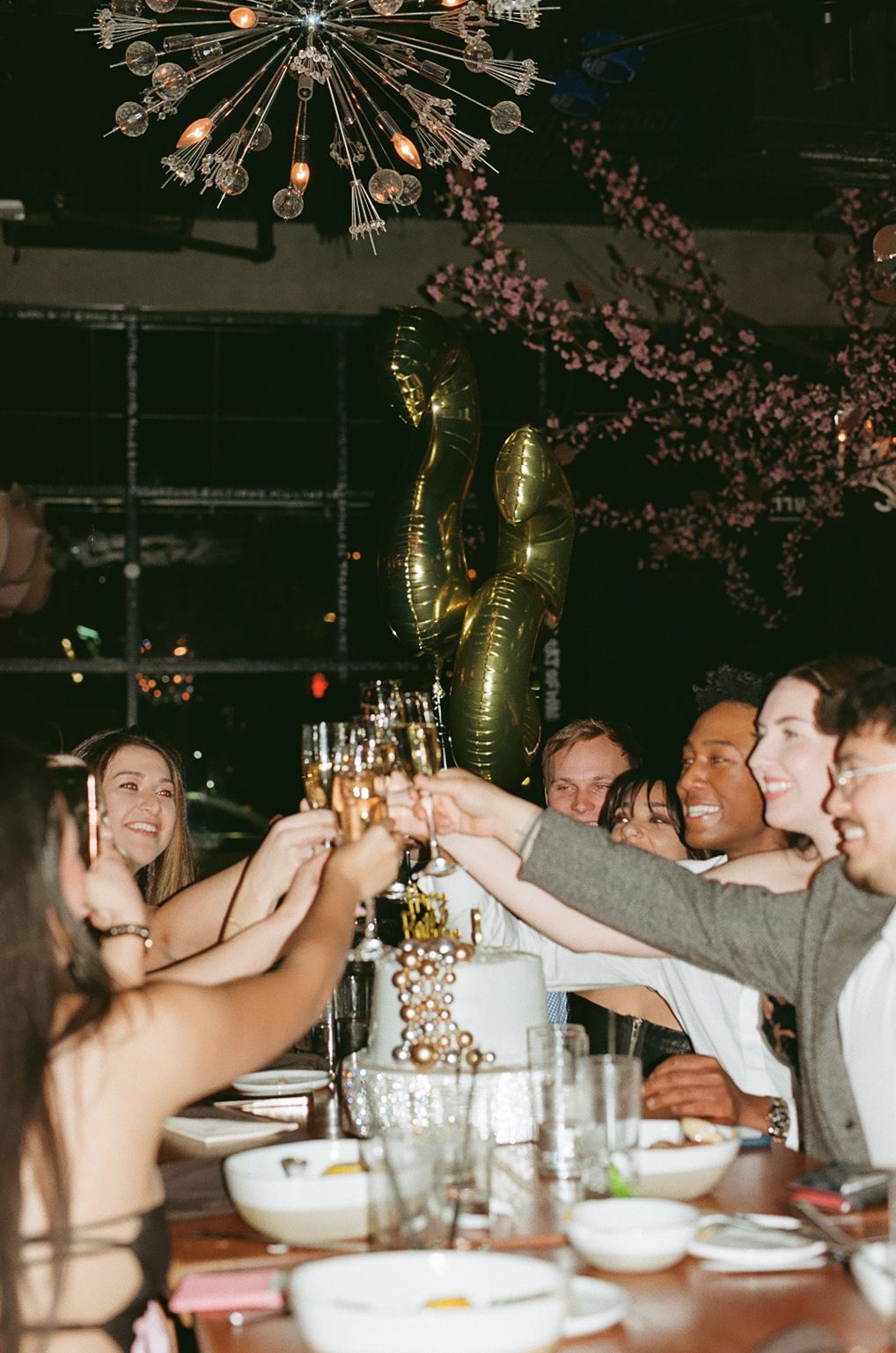 Friends toasting and celebrating at a dinner party under decorative lighting.