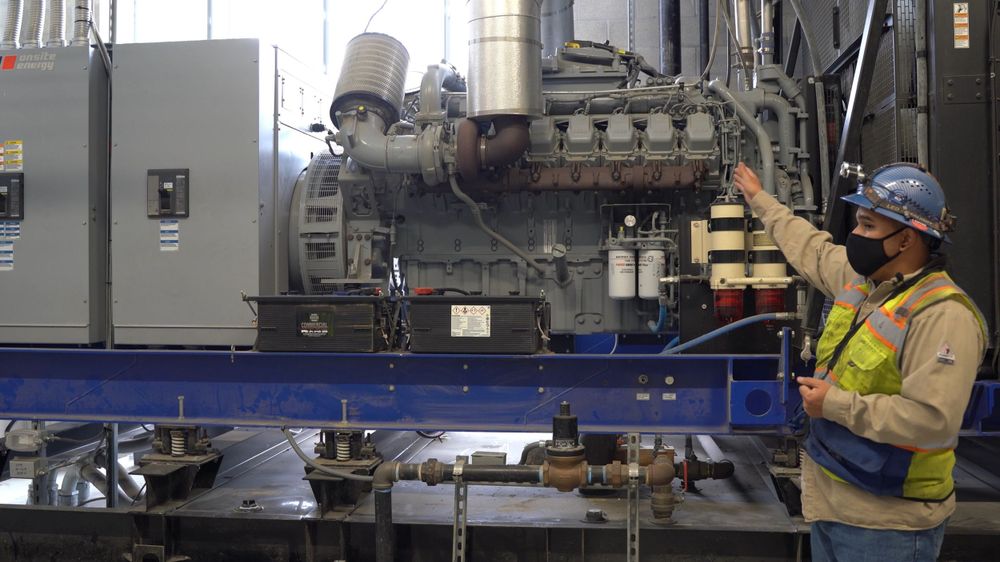 Facility engineer in high-visibility clothing showing the maintenance points on a large industrial power system.