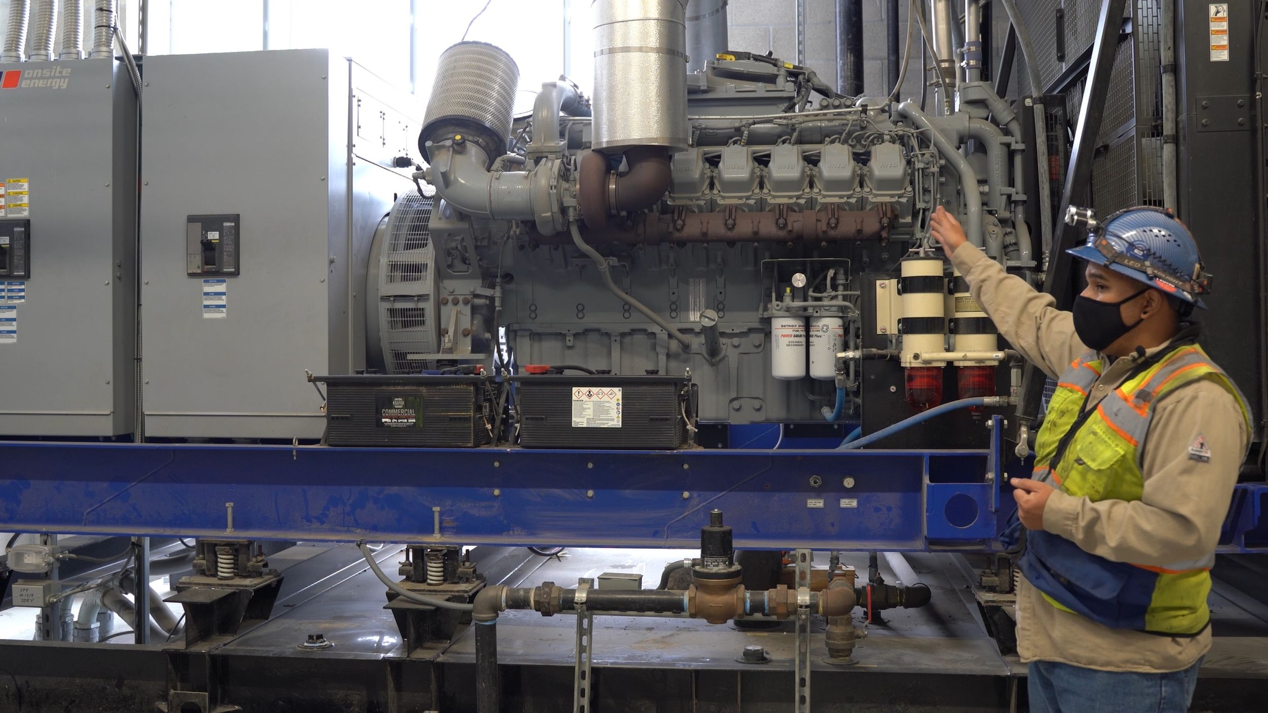 Facility engineer in high-visibility clothing showing the maintenance points on a large industrial power system.