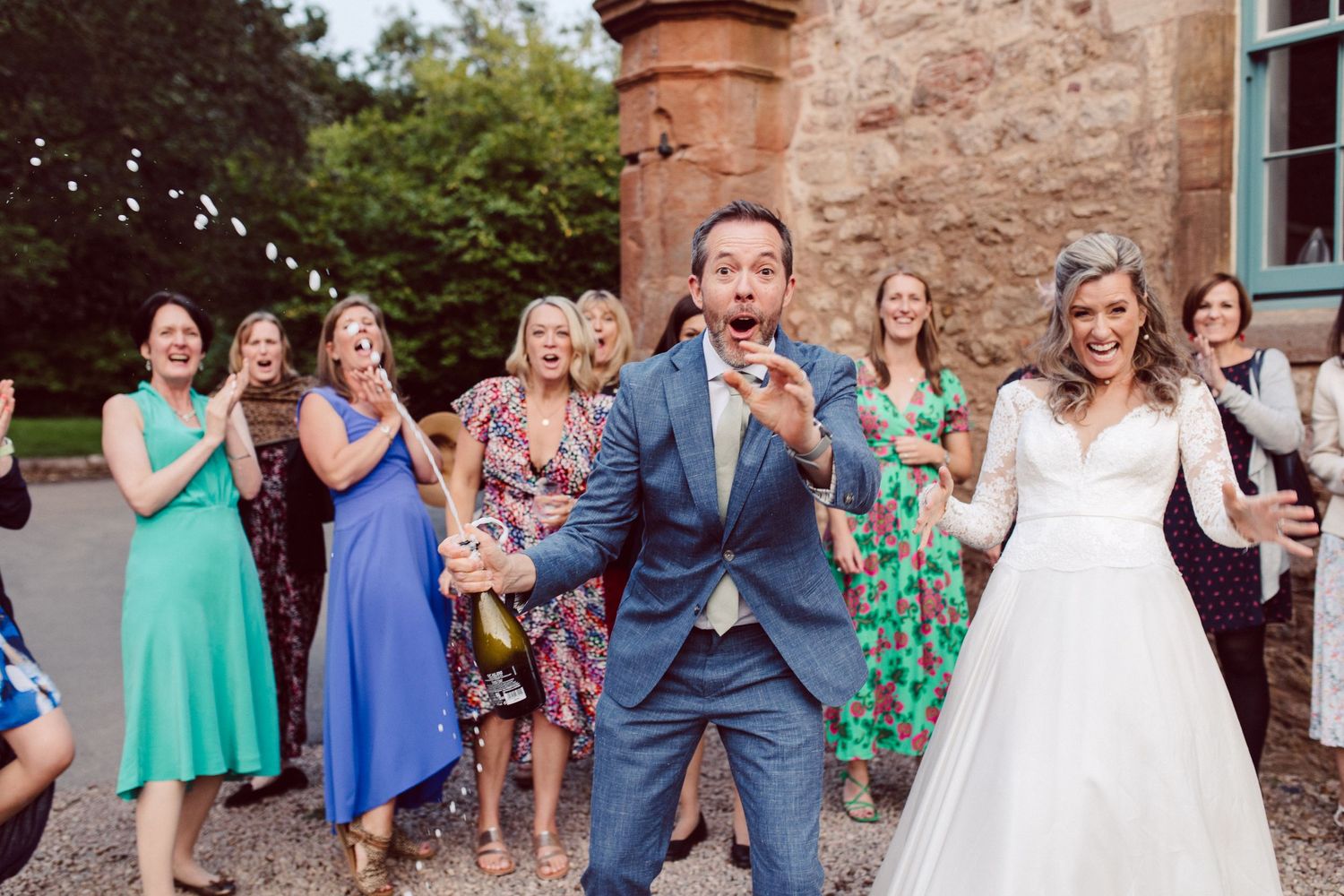 Wedding celebration with guests throwing confetti outside stone building.