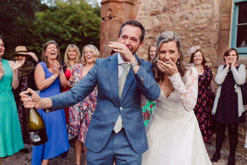 Joyful wedding celebration with guests cheering and throwing confetti outdoors.