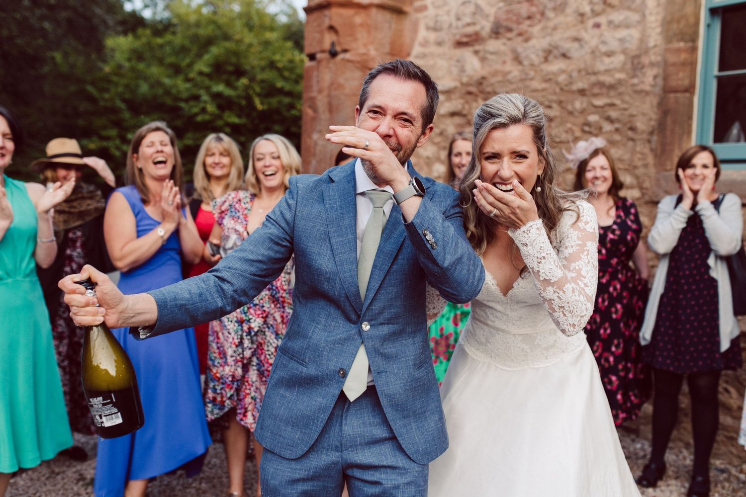 Joyful wedding celebration with guests cheering and throwing confetti outdoors.