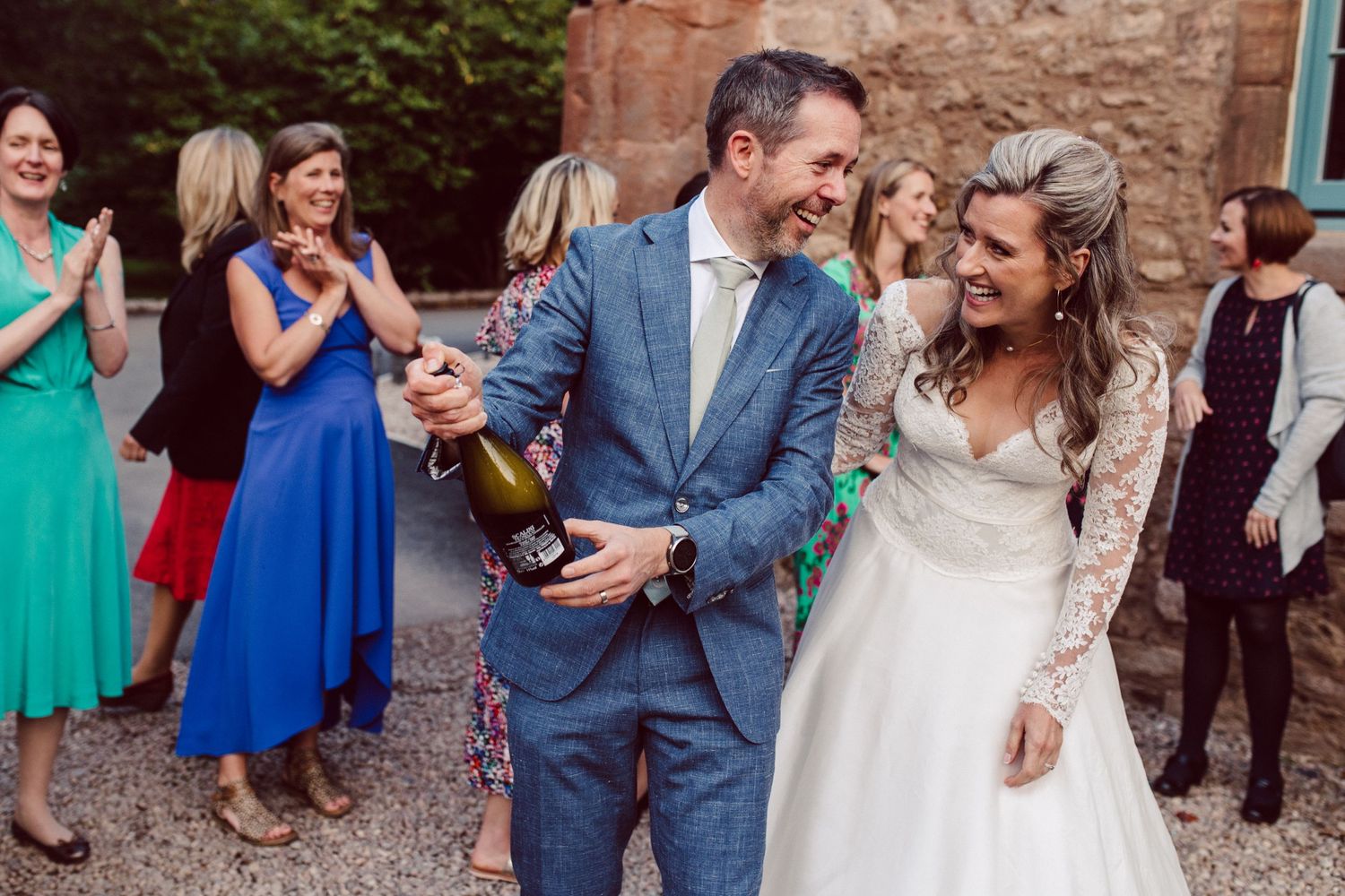 Wedding party celebrates with confetti toss outside historic stone venue.
