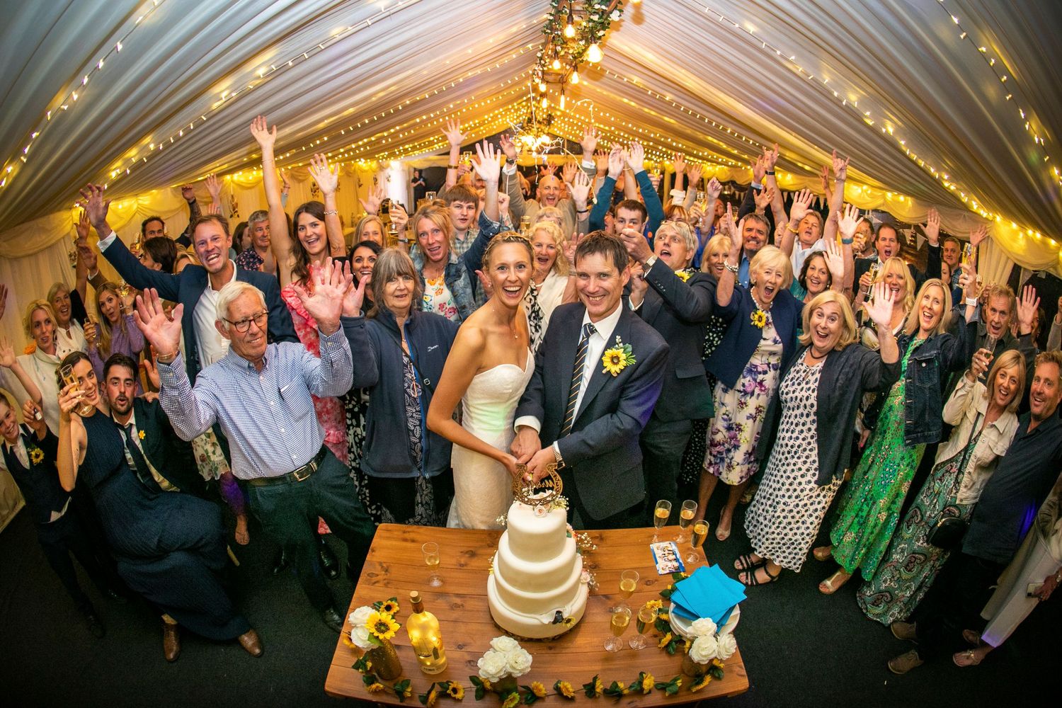 Wedding reception tent filled with guests celebrating under draped fabric and warm lighting.