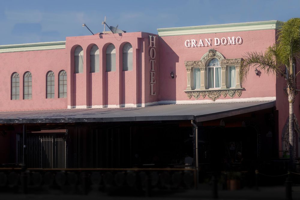 Pink exterior facade of Gran Domo hotel building with arched windows and palm tree.