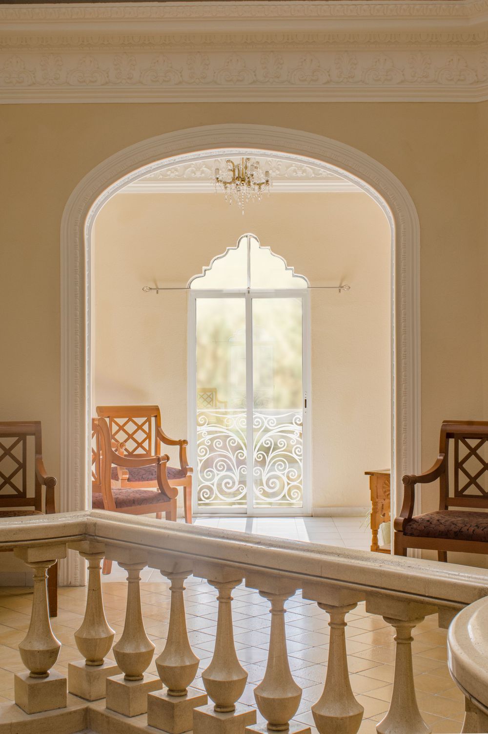 Elegant interior archway with white balustrade, chandelier, and ornate wrought iron balcony door.