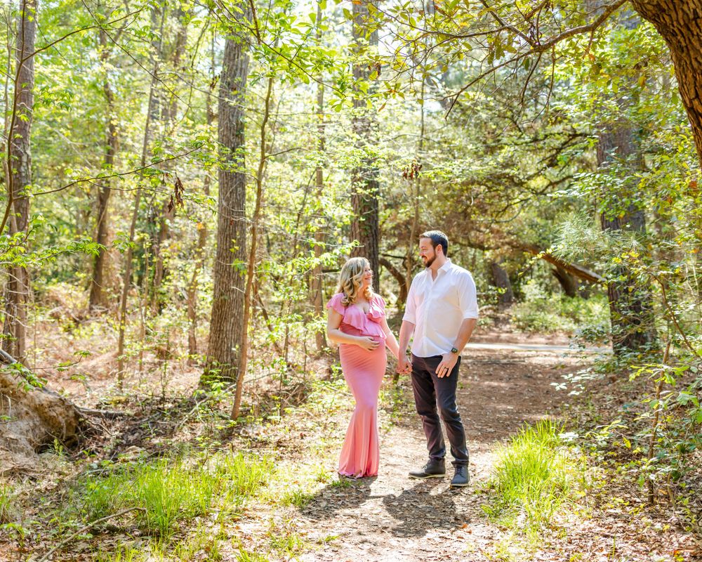 A couple walks along a sunlit forest path surrounded by green trees.