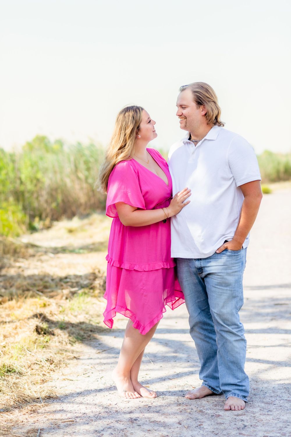 A couple stands barefoot on a sandy path wearing casual summer outfits.