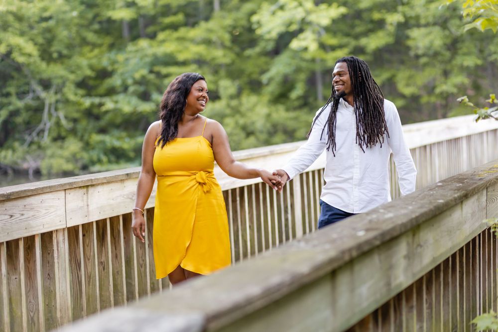 Two people share a happy moment while standing on a wooden bridge surrounded by lush greenery.