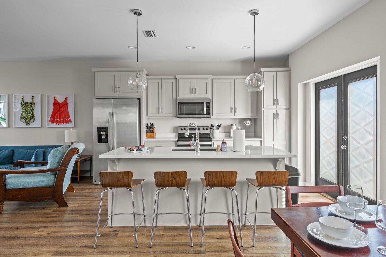 Contemporary kitchen featuring white cabinets, wooden bar stools, and blue accent seating.