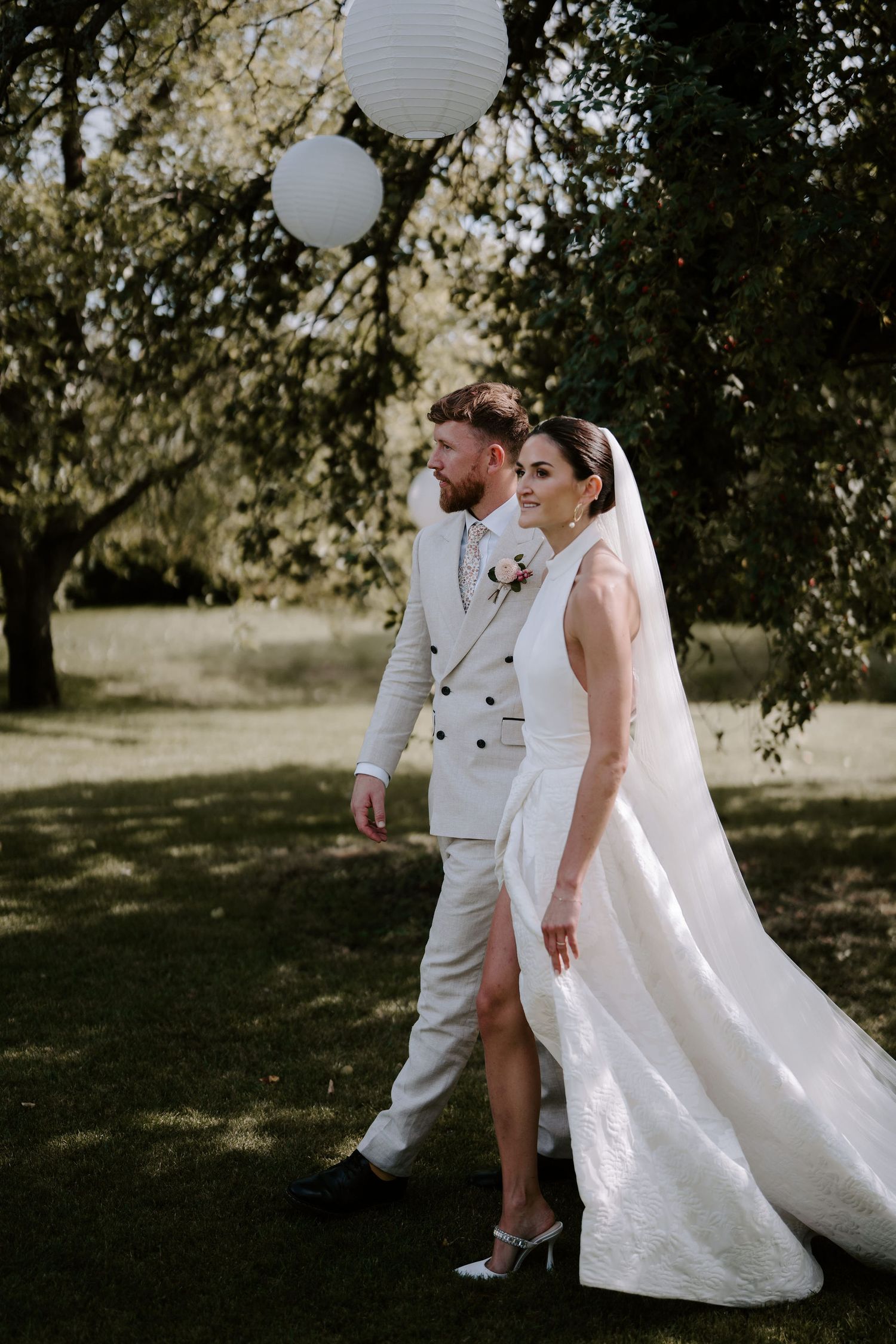 bride and groom walking under lanterns hung from a willow tree in islip, oxfordshire