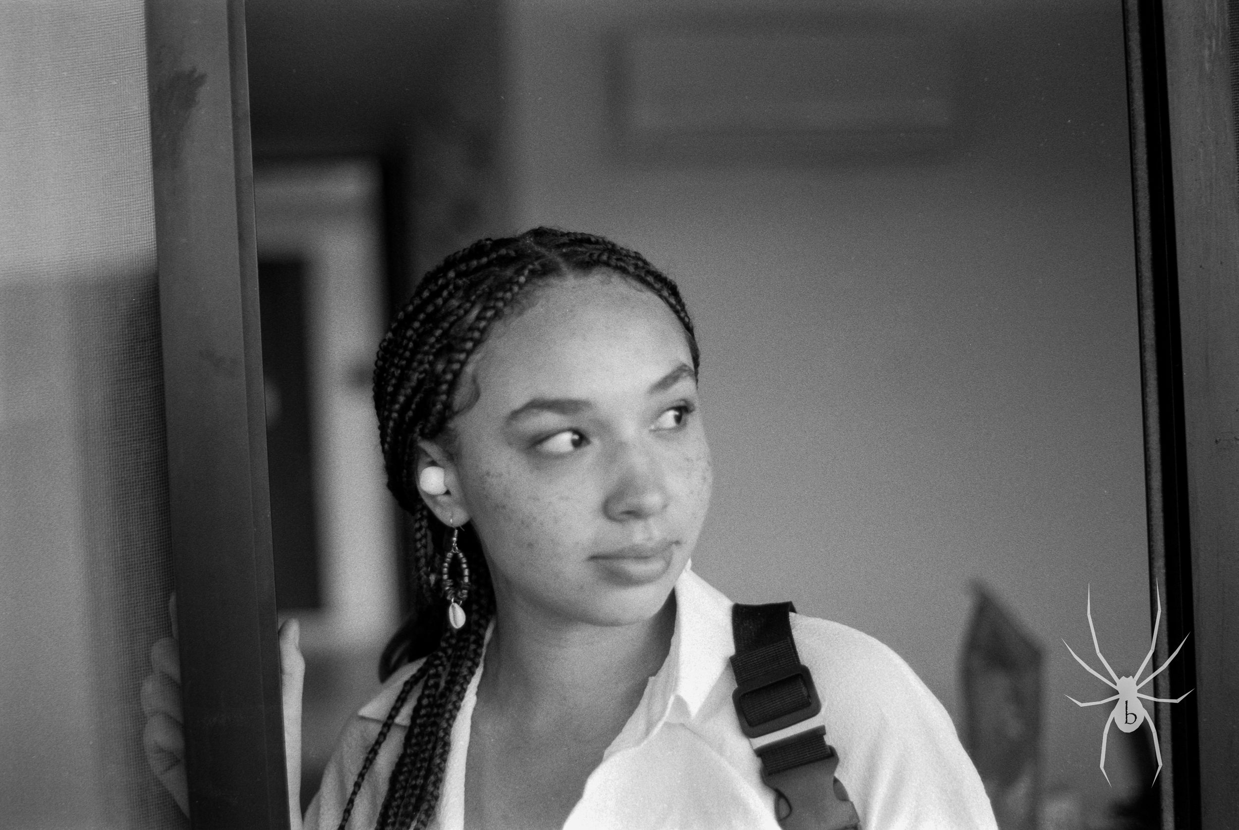 Black and white portrait of a person with braided hair wearing a white shirt and earrings.